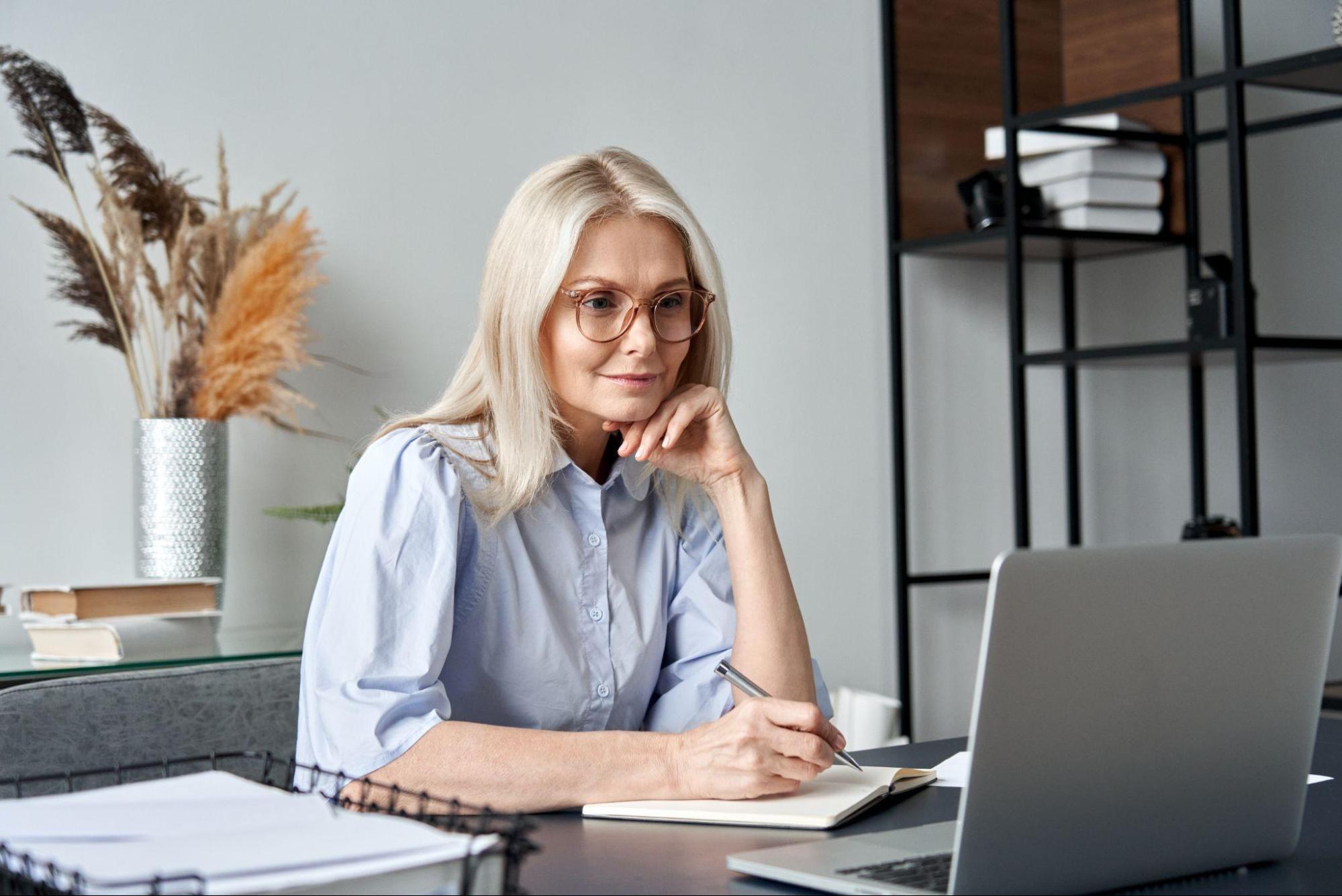 A woman writes in a notepad in front of a laptop computer.