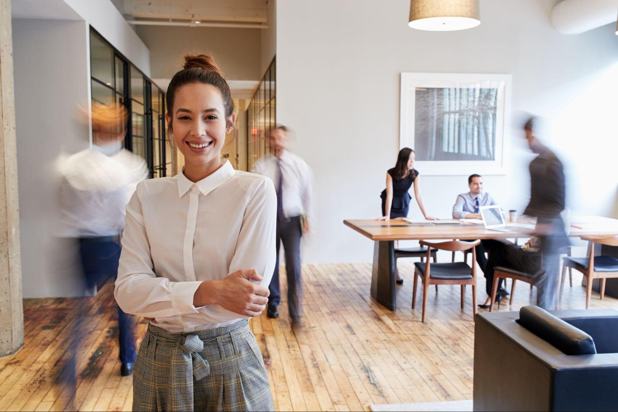 A focused young woman in a bustling modern office environment.