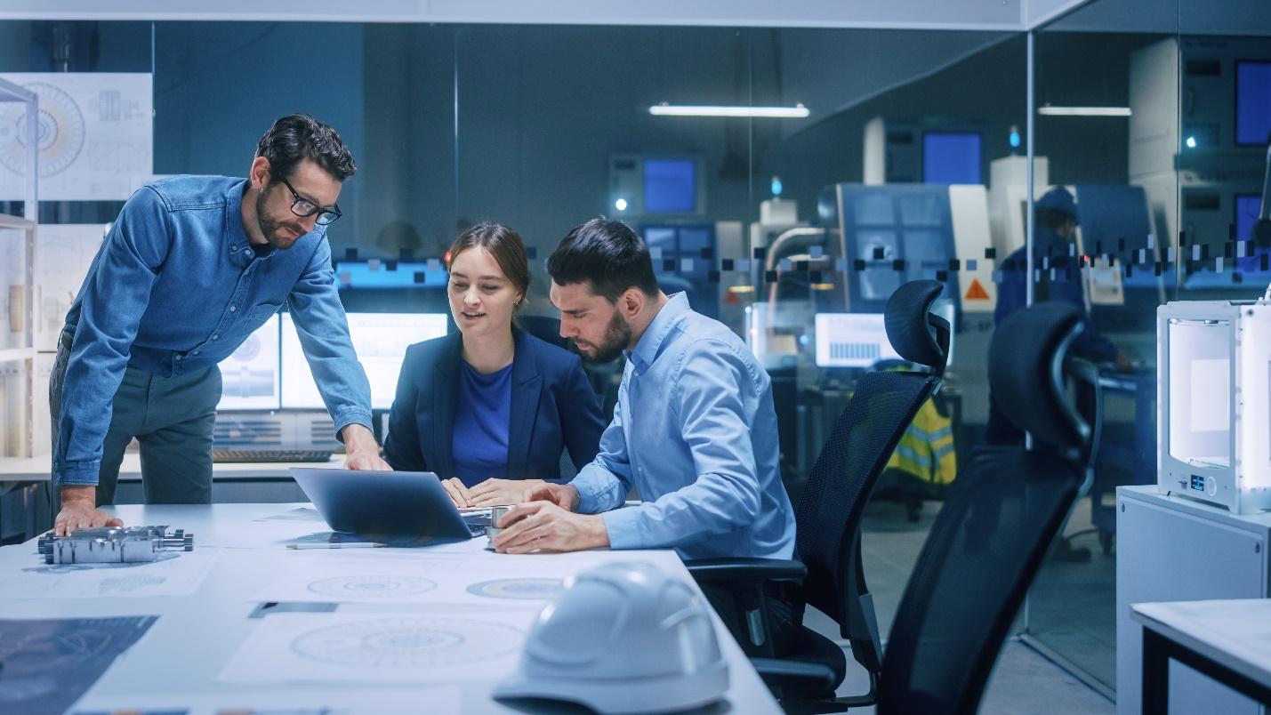 Three IT professionals gather around a laptop on an office conference table.